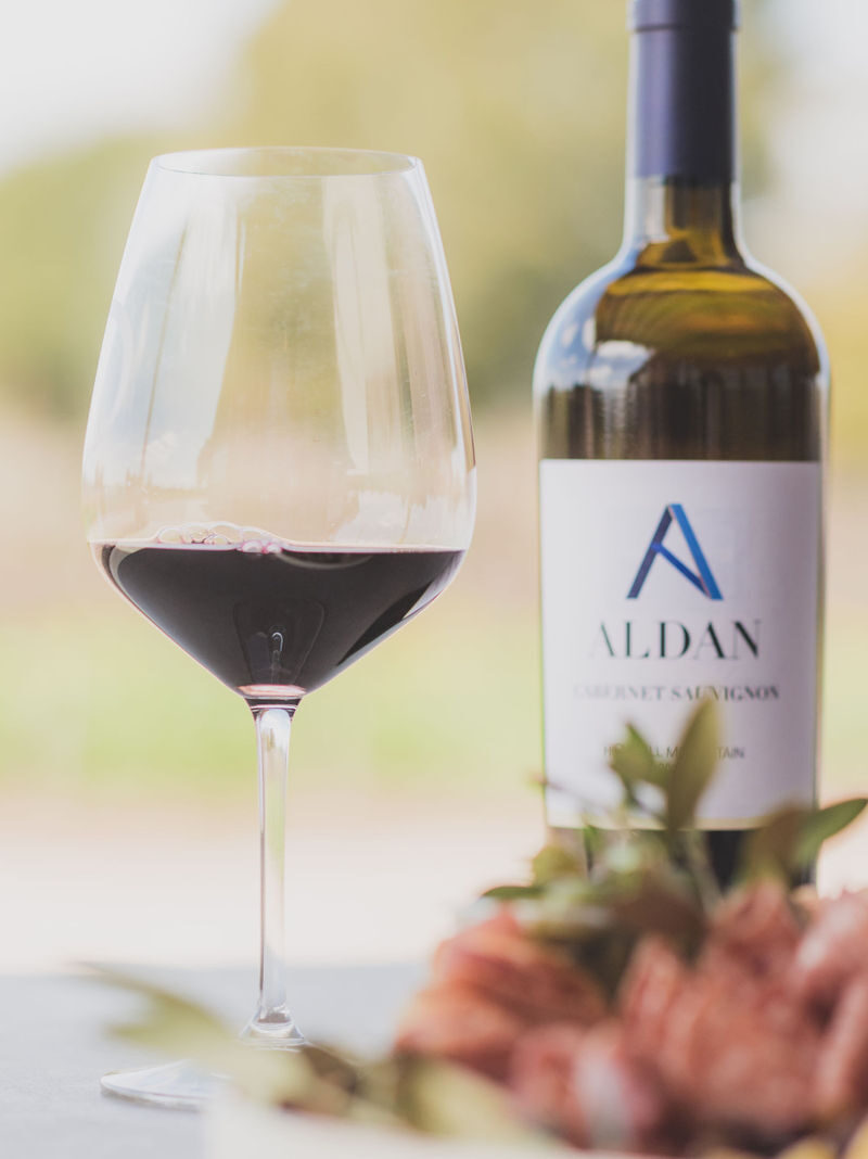 ALDAN wine bottle behind a glass of red wine