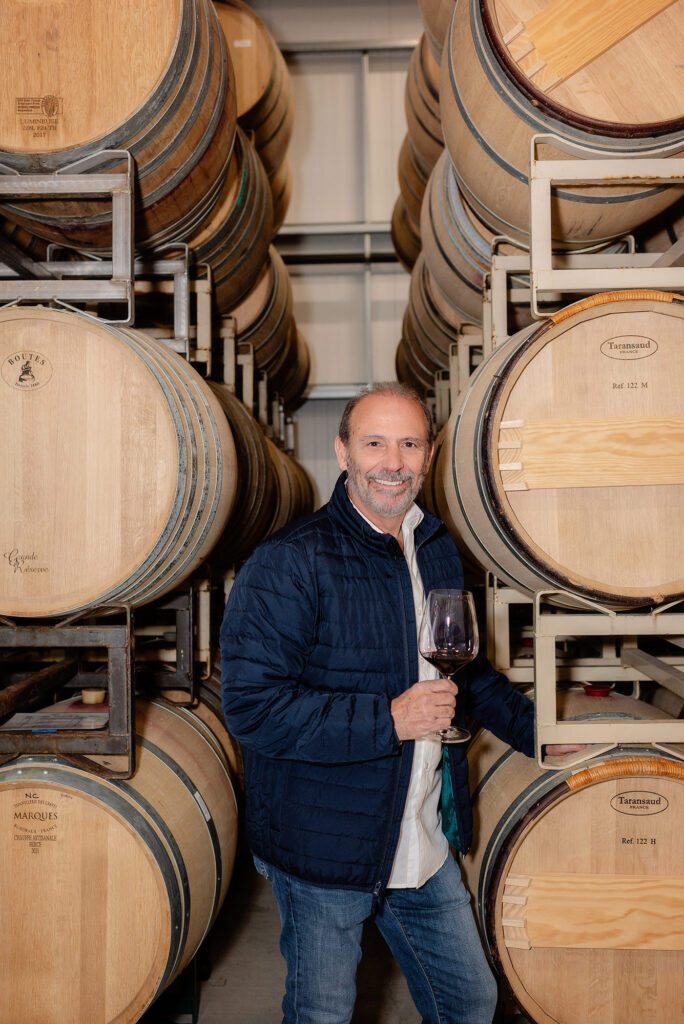 ALDAN Wines owner Alfredo Vega between racks of barrels holding a glass of wine