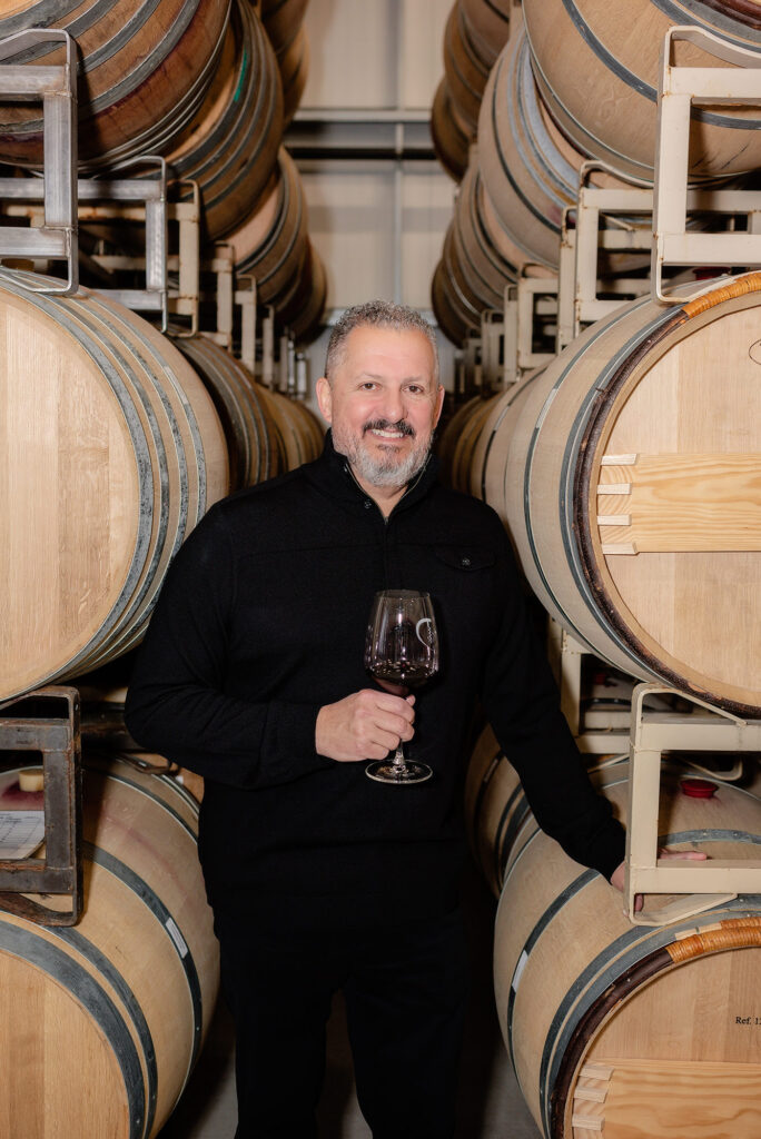 ALDAN Wines owner Danny Borrego between racks of barrels holding a glass of wine